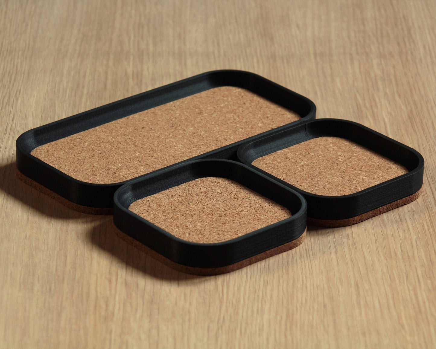 Three black rectangular desk trays with a natural cork bottom, set on a wooden surface.