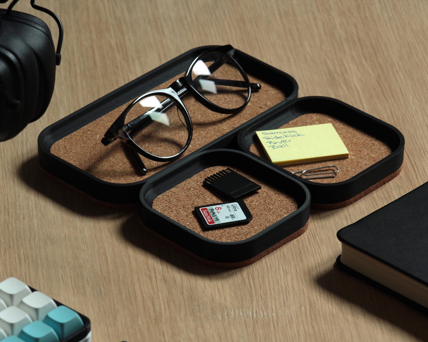 A set of three matte-black desk trays with thick cork base and top cork lining, sitting on a white oak desk
