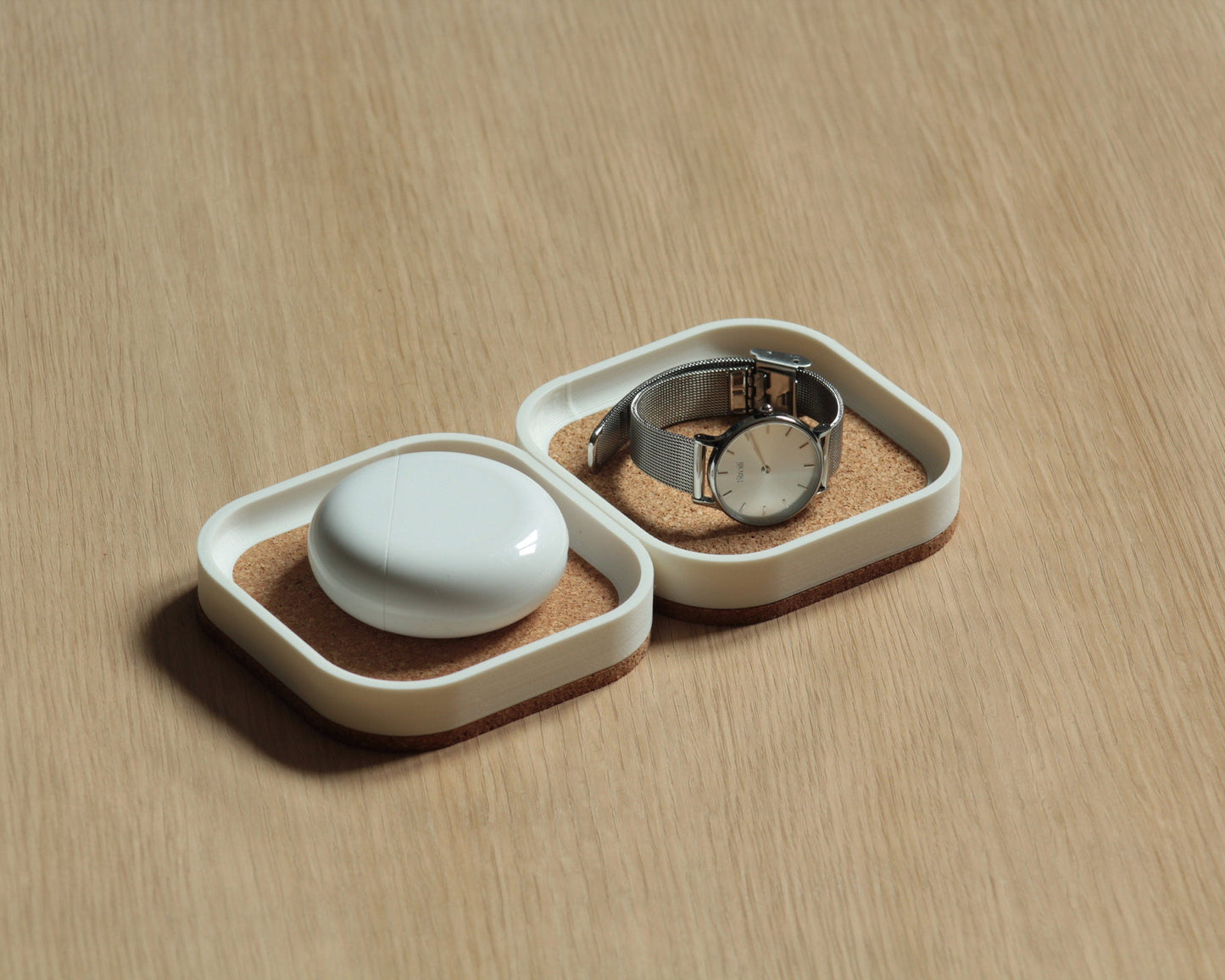 Two small square catch-all trays in matte white color with cork lining at the top and a thick cork base, on a light wooden surface