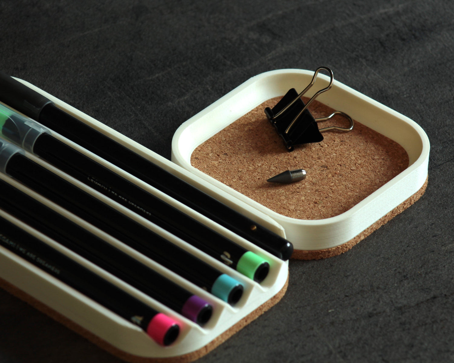 Photo of two matte white valet trays with thick cork base on a dark desk surface