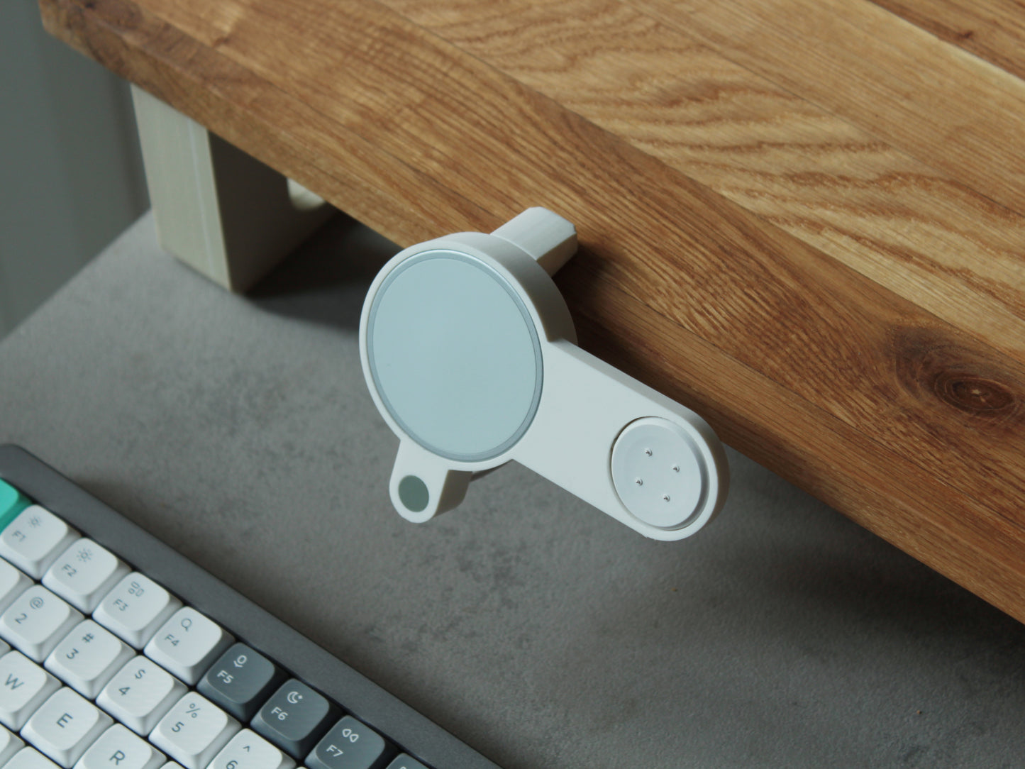 Photo of NODO Lite holder compatible with Google Pixelsnap and Pixel Watch 2 & 3 charger holder clamped on an oak desk shelf. The holder is made of matte white color with a sage green accent dot