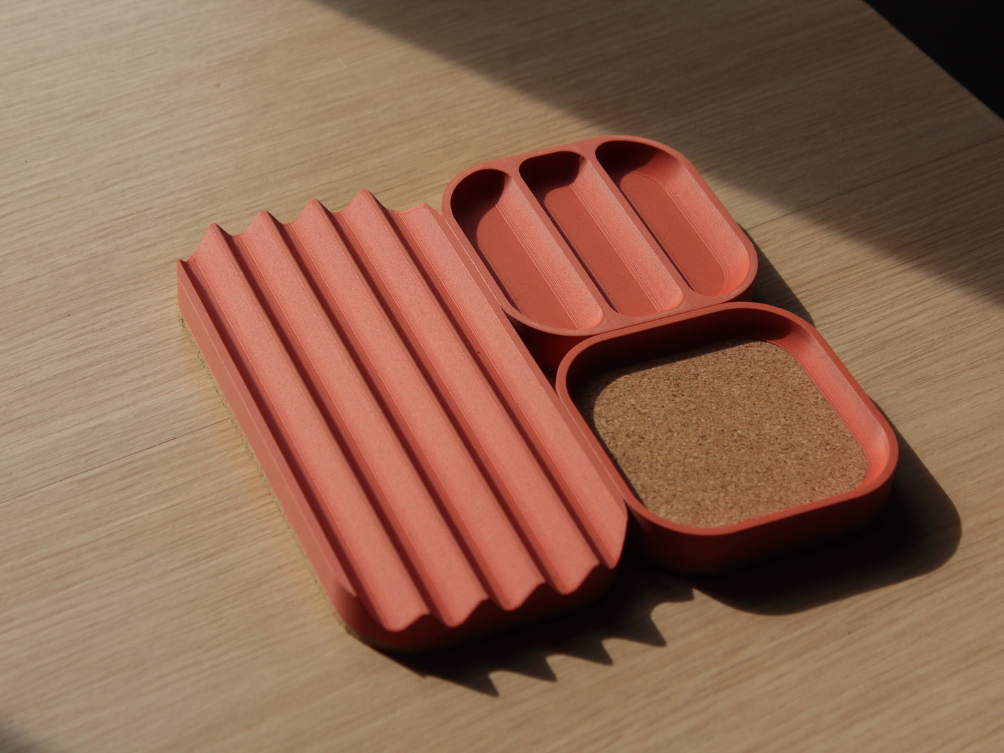 A set of brick orange modular trays with rounded corners and cork padding. There are 2 small square trays and a longer one with V-shaped slots for storing pens and markers