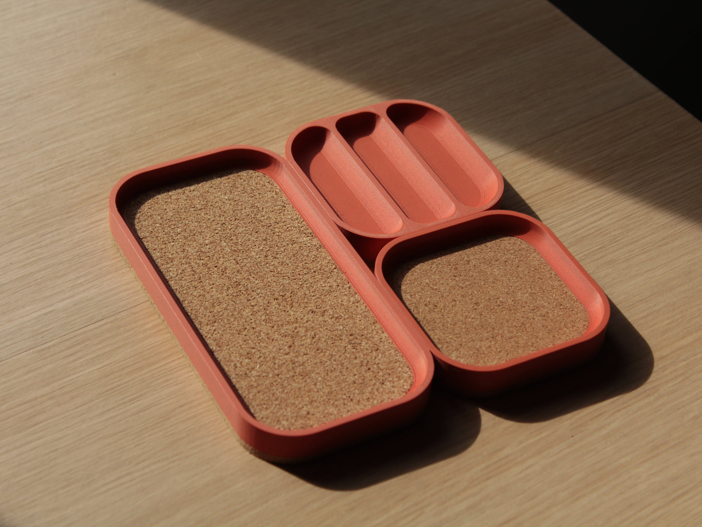 A set of brick orange modular trays with rounded corners and cork padding. There are 2 small square trays and a longer one with a cork-padded pocket